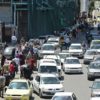 In this file photo taken on May 10, 2020, pedestrians walk along a line of cars in a busy street in the Syrian capital Damascus