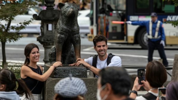 A couple pose for photos next to the statue of 'Hachiko' in front of Tokyo's Shibuya station