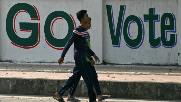Men walk past a wall writing urging people to vote in Dhaka on January 6, 2024, on the eve of Bangladesh's general election