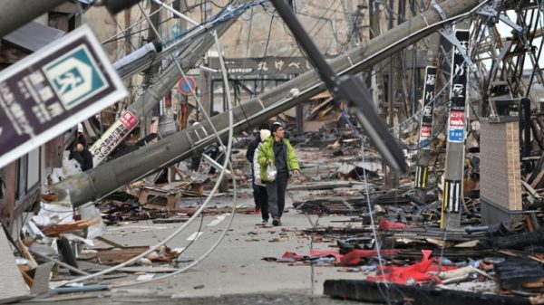 People walk past fallen utility poles and damaged buildings in the city of Wajima, Ishikawa prefecture